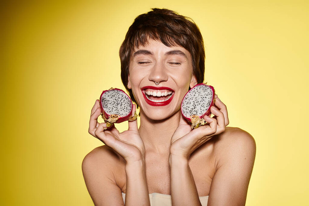 A woman playfully holds two dragon fruits in front of her face. - Photo, Image