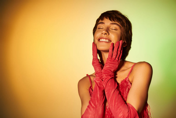 Une femme gracieuse en gants rouges se tient debout les yeux fermés sur une toile de fond vibrante. - Photo, image