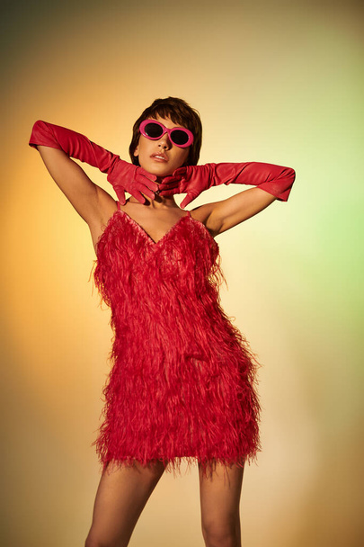 Uma jovem elegante faz uma pose em um vestido vermelho vibrante e óculos de sol elegantes. - Foto, Imagem