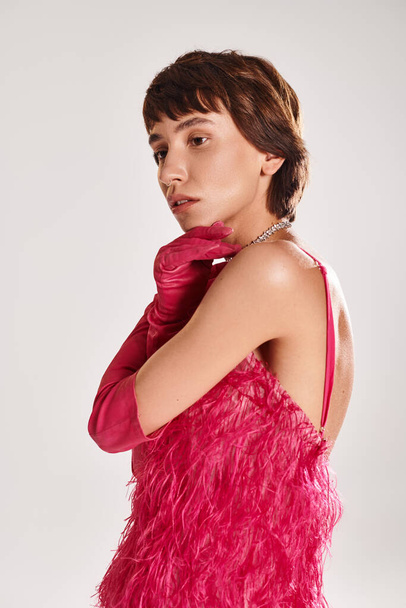 Jeune femme en robe de plume rose frappe une pose sur fond vibrant. - Photo, image