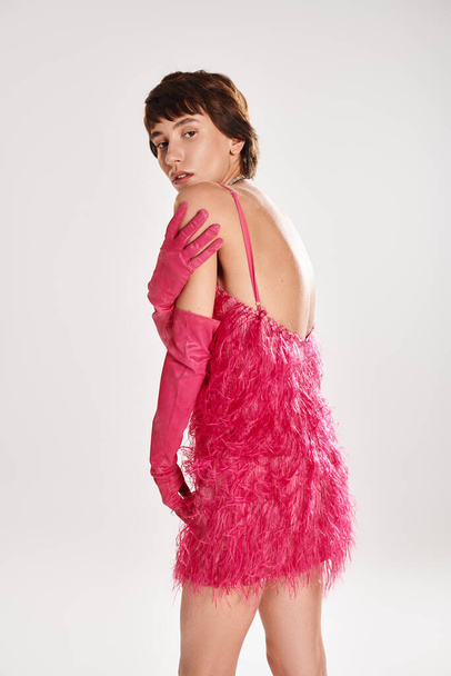 Eine modische junge Frau posiert in einem eleganten rosa Kleid und Handschuhen vor einem lebendigen Hintergrund. - Foto, Bild