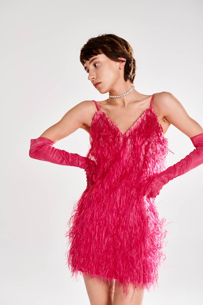 Модная молодая женщина позирует в элегантном розовом платье с перьями на ярком фоне. - Фото, изображение