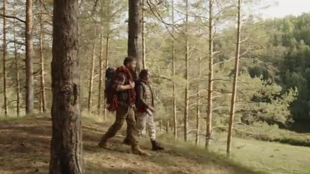 PAN foto de una joven pareja de turistas caminando a través de bosques de pinos y mirando la impresionante vista de la montaña cubierta de bosque y río - Imágenes, Vídeo