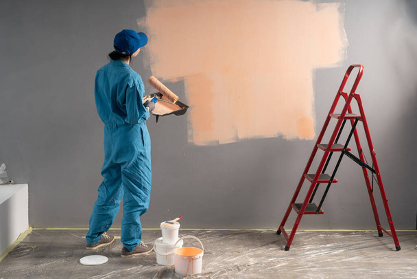 Γυναίκα ζωγράφος στέκεται με ρολό χρώμα κοιτάζοντας άδειο τοίχο ή χώρο για κείμενο, πίσω όψη. Αντιγραφή χώρου - Φωτογραφία, εικόνα