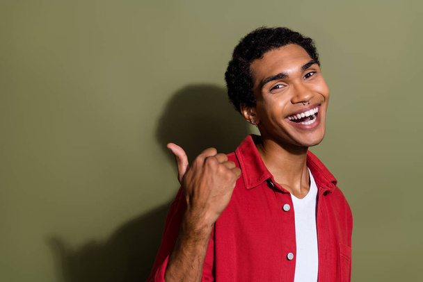Photo of positive excited guy wear red shirt pointing thumb back empty space isolated khaki color background. - Foto, imagen