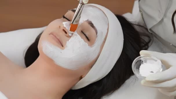 Anti-Aging-Hautpflege mit Gesichtsmaske: Verbessert den Zustand und das Aussehen der Haut, indem sie Falten reduziert und die Gesichtskontur einer Frau in einem Schönheitssalon mit einer Kosmetikerin strafft. Hohe Qualität 4k - Filmmaterial, Video