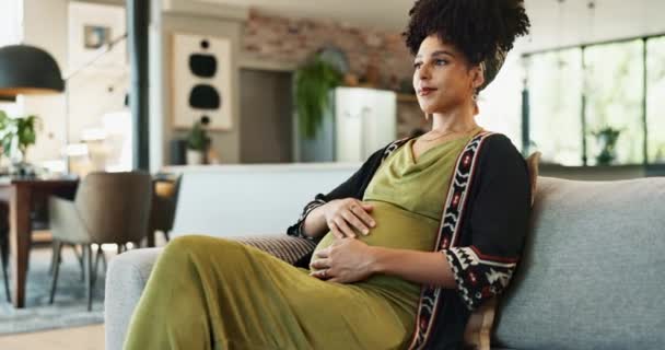 Black woman, pregnant and home on sofa thinking with excitement for baby, thoughts and love for belly with happiness. Future mother, hold stomach and couch, wondering with ideas for maternity care - Footage, Video