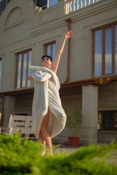 Девушка, завернутая в одеяло, танцует на улице, наслаждаясь утренними ритуалами. Оживленное начало дня с кафе неподалеку. - Фото, изображение