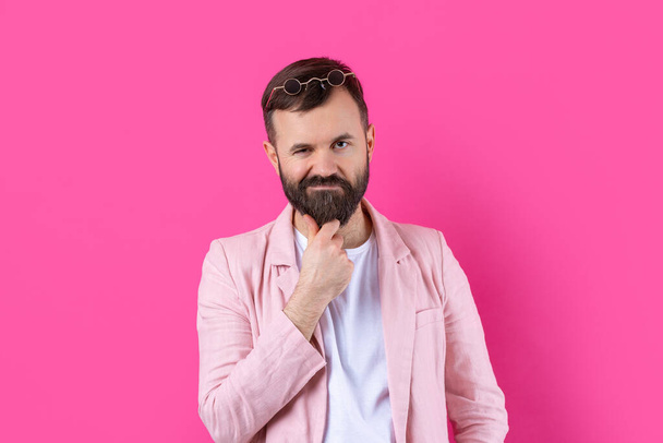 Homem barbudo vestido com um casaco cor-de-rosa com óculos. Retrato de estúdio emocional. - Foto, Imagem