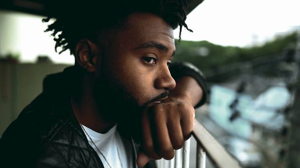 Yksi intensiivinen heijastus nuori musta mies 20s nojaten parveke baarissa tuijottaen kaupunkinäkymät syvä meditatiivinen mietiskelyä. Afrikkalainen amerikkalainen henkilö hiljaisessa yksinäisyydessä - Valokuva, kuva