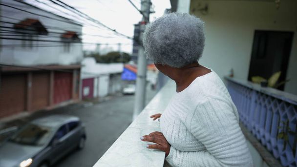 Jedna postarší jihoamerická žena pozorující okolí z balkónu rezidence. 80. léta senior osoba dívá na městské ulice shora se šťastným výrazem - Fotografie, Obrázek