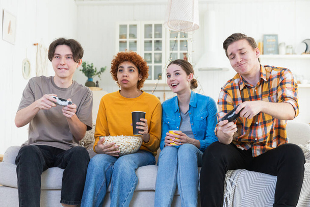 ホームパーティー。 自宅でビデオゲームをする友人の陽気なグループ. ハッピーな多様なグループの仲間が一緒に屋内で楽しんでいます. 友情レジャーエンターテイメントコンセプト。 週末を楽しんでいる若い親友 - 写真・画像