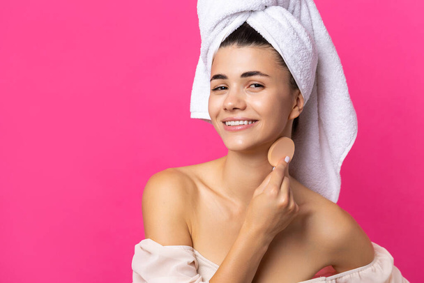 Mooi vrolijk aantrekkelijk meisje met een handdoek op haar hoofd, houdt een spons tegen een roze achtergrond. - Foto, afbeelding
