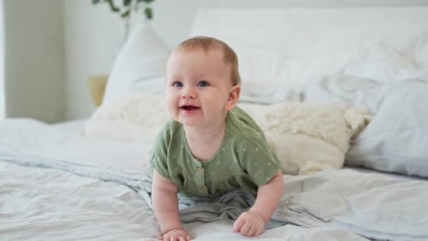 ハッピーベイビー。 ベッドルームのベッドで笑顔でかわいい小さな新生児. 赤ん坊は家で毛布の上に横たわって遊んでいます. 母性幸せな育児コンセプト - 映像、動画