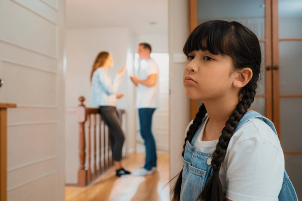 Stressed and unhappy young girl huddle in corner crying and sad while her parent arguing in background. Domestic violence at home and traumatic childhood develop to depression. Synchronos - Photo, Image