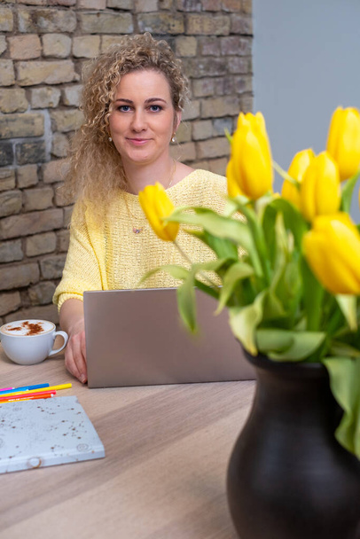 Das helle Ambiente eines kreativen Arbeitsplatzes wird von einer Frau mit freundlichem Auftreten eingefangen, umgeben von fröhlichen Tulpen, die eine blühende Karriere oder ein blühendes Geschäft symbolisieren. Hochwertiges Foto - Foto, Bild
