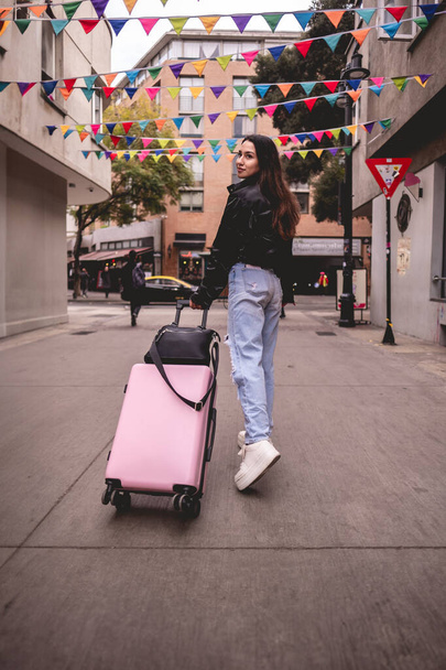 Стильні подорожі та дослідження міст: яскрава молода латиноамериканська брюнетка з модним виглядом та рожевою валізою, що досліджує історичний район міста та центру - Фото, зображення