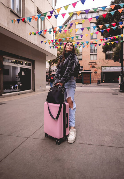 Stylish travel and urban exploration: vibrant young latina brunette with fashion look and pink suitcase exploring city historic district and downtown - Photo, Image