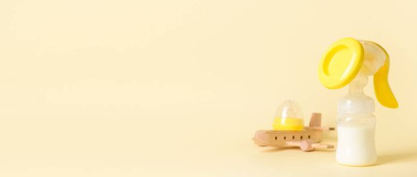 Грудний насос та дитяча іграшка на світло-жовтому фоні з місцем для тексту - Фото, зображення