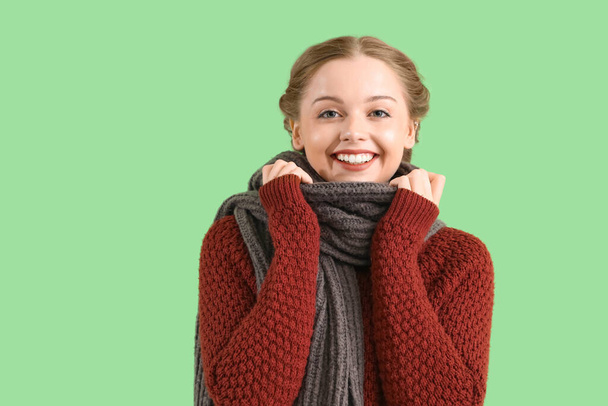 Красива щаслива молода жінка в теплому светрі і шарфі на зеленому фоні - Фото, зображення
