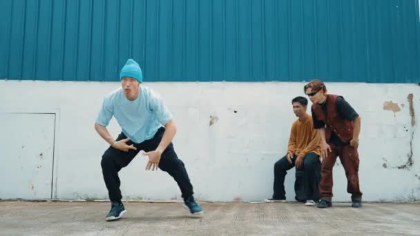 Mladý pouliční tanečník tančí ve stylu hip hopu s multikulturními přáteli, kteří jásají za zdí. Atraktivní pohledný muž natahuje ruce na ulici s modrým pozadím. Outdoor sport 2024. hiphop. - Záběry, video