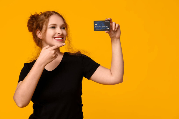 Beautiful young woman pointing at credit card on yellow background - Photo, Image