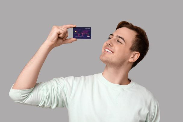 Joven con tarjeta de crédito sobre fondo gris - Foto, Imagen