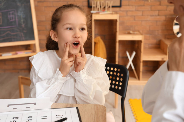 Petite fille mignonne avec orthophoniste prononçant des lettres à la table au bureau - Photo, image
