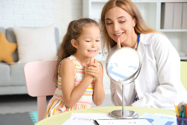 Mature speech therapist working with little girl near mirror at table in office - Foto, imagen