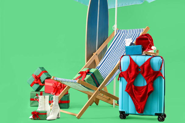 Matkalaukku kansituoli, surffilauta ja lahjapakkaukset vihreällä taustalla. Talviloma käsite - Valokuva, kuva