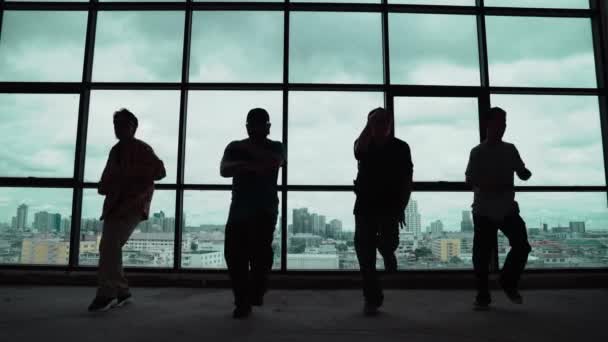 Silhouette lövés képzett koreográfus csoport táncol együtt ég scrapper vagy városkép háttér. A fiatal hipszter csapat táncol az ablak közelében. Szabadtéri sport 2024. hiphop. - Felvétel, videó