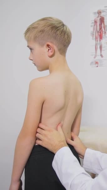 Egy szőke fiú, egy iskolás, akit megvizsgál egy ortopéd orvos. Egy profi ortopéd megvizsgálja a fiúkat. A gerincferdülés megelőzése és kezelése gyermekeknél - Felvétel, videó