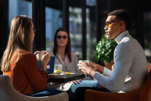 Three friends in a restaurant talking smiling and drinking tea. Business colleagues having a meeting after work or during coffee break at a cafe bar. - Fotoğraf, Görsel