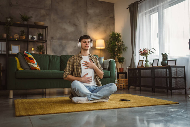 Een tiener man doet begeleide meditatie yoga zelfzorg praktijk thuis - Foto, afbeelding