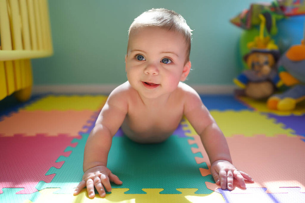 Adorable smiling cute funny happy infant baby in diaper crawling and playing on the floor on a developing foam puzzle play mat with toys in nursery room. Healthy child concept. Baby goods packaging - Photo, Image