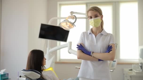 Naispuolinen hammaslääkäri, joka on pukeutunut käsineisiin ja naamioon, hoitaa potilasta hammastuolissa korostaen sitoutumistaan laadukkaiden hammashoitopalvelujen tarjoamiseen.. - Materiaali, video