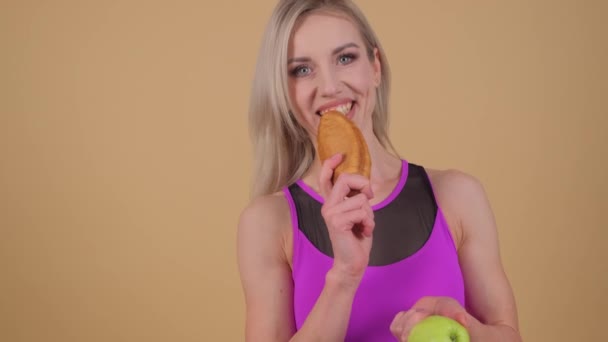 De blonde vrouw is gelukkig genieten van haar eten, met een glimlach op haar gezicht terwijl ze een appel in de ene hand en een sandwich in de andere hand. - Video