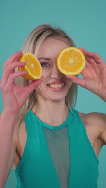 Una mujer feliz con una sonrisa sostiene dos rodajas de limón dulce, una fruta cítrica, frente a sus ojos como un gesto juguetón. - Metraje, vídeo