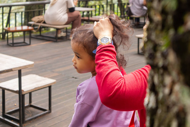 Blick auf die Hand einer Mutter, die ihrer Tochter im Freien die Haare bindet. Ein asiatisches kleines Mädchen. - Foto, Bild