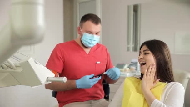 Μια γυναίκα κάθεται σε μια οδοντιατρική καρέκλα καθώς ένας οδοντίατρος εξετάζει τα δόντια της, χρησιμοποιώντας το χέρι και τα δάχτυλά τους για να ελέγξει το χαμόγελό της, το στόμα, και τους μυς της. - Πλάνα, βίντεο