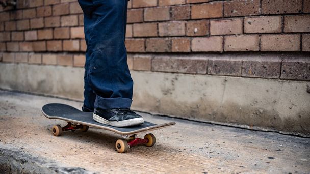 Uma imagem de perto de pés de um patinador macho montado em um skate na rua. Pernas de patinador ativas irreconhecíveis praticando skate em uma rua da cidade. - Foto, Imagem