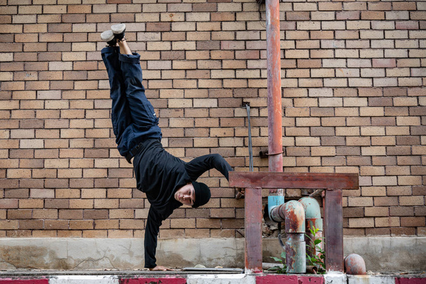 A professional, active Asian male hip-hop breakdancer is dancing on the street in the city, standing on one hand, showcasing his talented movements. - Photo, Image