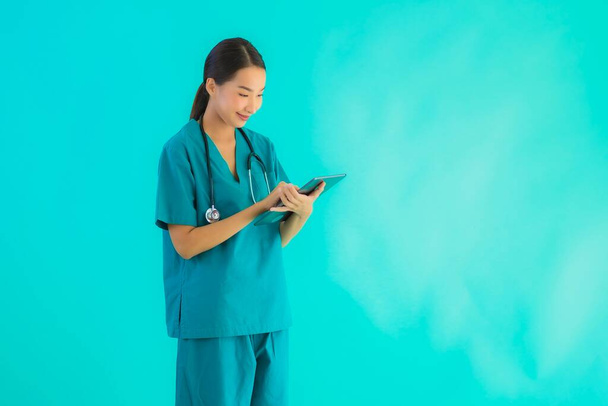 Retrato bonito jovem asiático médico mulher uso inteligente tablet dispositivo no azul isolado fundo
 - Foto, Imagem