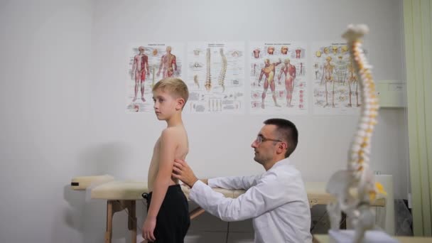 Behandeling van scoliose bij kinderen. Orthopedische dokter onderzoekt de rug van een kleine jongen. Kinderarts. - Video