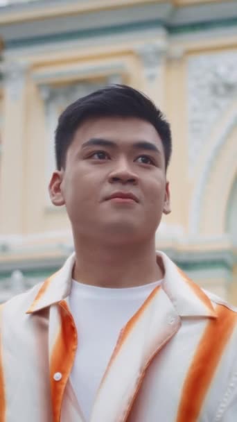 Vertikales Porträt eines lächelnden asiatischen Gen Z-Typen, der in die Kamera schaut, wenn er in der Innenstadt spaziert - Filmmaterial, Video