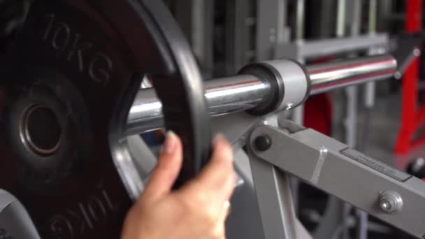 Close-up of dumbbells for strength training. A womans hand puts a circle of dumbbells on a bar. - Footage, Video