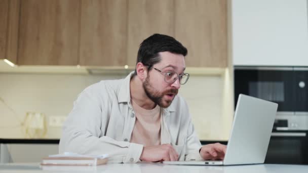 Kafkasyalı erkek, ahşap mutfak arka planındaki kişisel dizüstü bilgisayarına bakarak olumlu jestler yapıyor. Mesai arasında online piyango kazanan mutlu bir adam.. - Video, Çekim