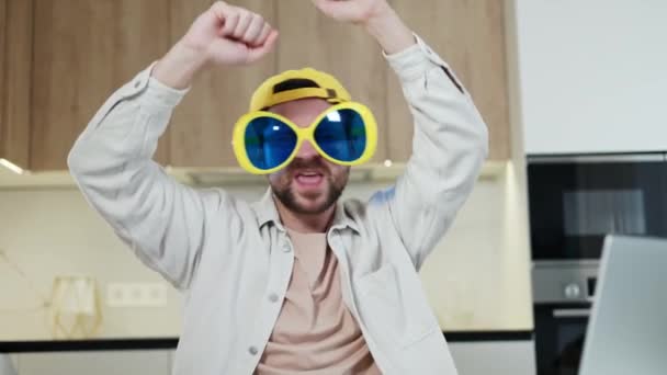 Απρόσεκτος άνθρωπος φορώντας funky γυαλιά κόμμα και κίτρινο καπέλο, ενώ κάνει το χορό νικητής στην εγχώρια χώρο εργασίας. Χαρούμενος μακρινός project manager που γιορτάζει την επιτυχία με ρυθμικές κινήσεις και παλαμάκια. - Πλάνα, βίντεο