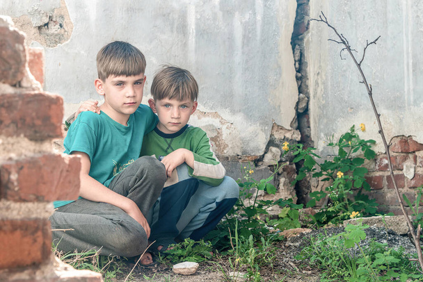 Παιδιά σε ένα εγκαταλελειμμένο σπίτι, δύο φτωχά εγκαταλειμμένα αγόρια, ορφανά ως αποτέλεσμα φυσικών καταστροφών και στρατιωτικών ενεργειών. Φωτογραφία υποβολής. - Φωτογραφία, εικόνα