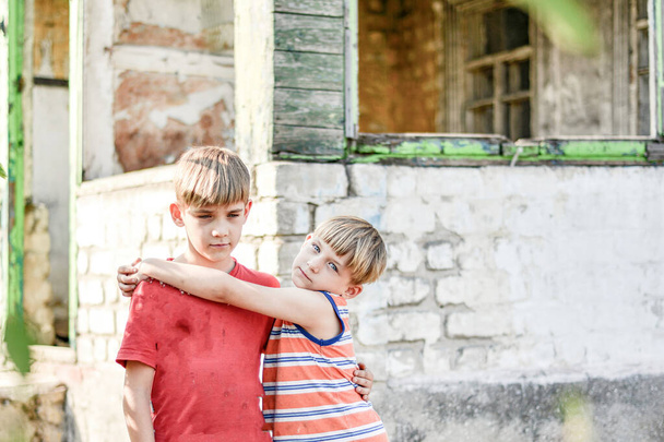 Два брата стоят возле сгоревшего дома, потерявшего свои дома в результате военных действий и стихийных бедствий
. - Фото, изображение